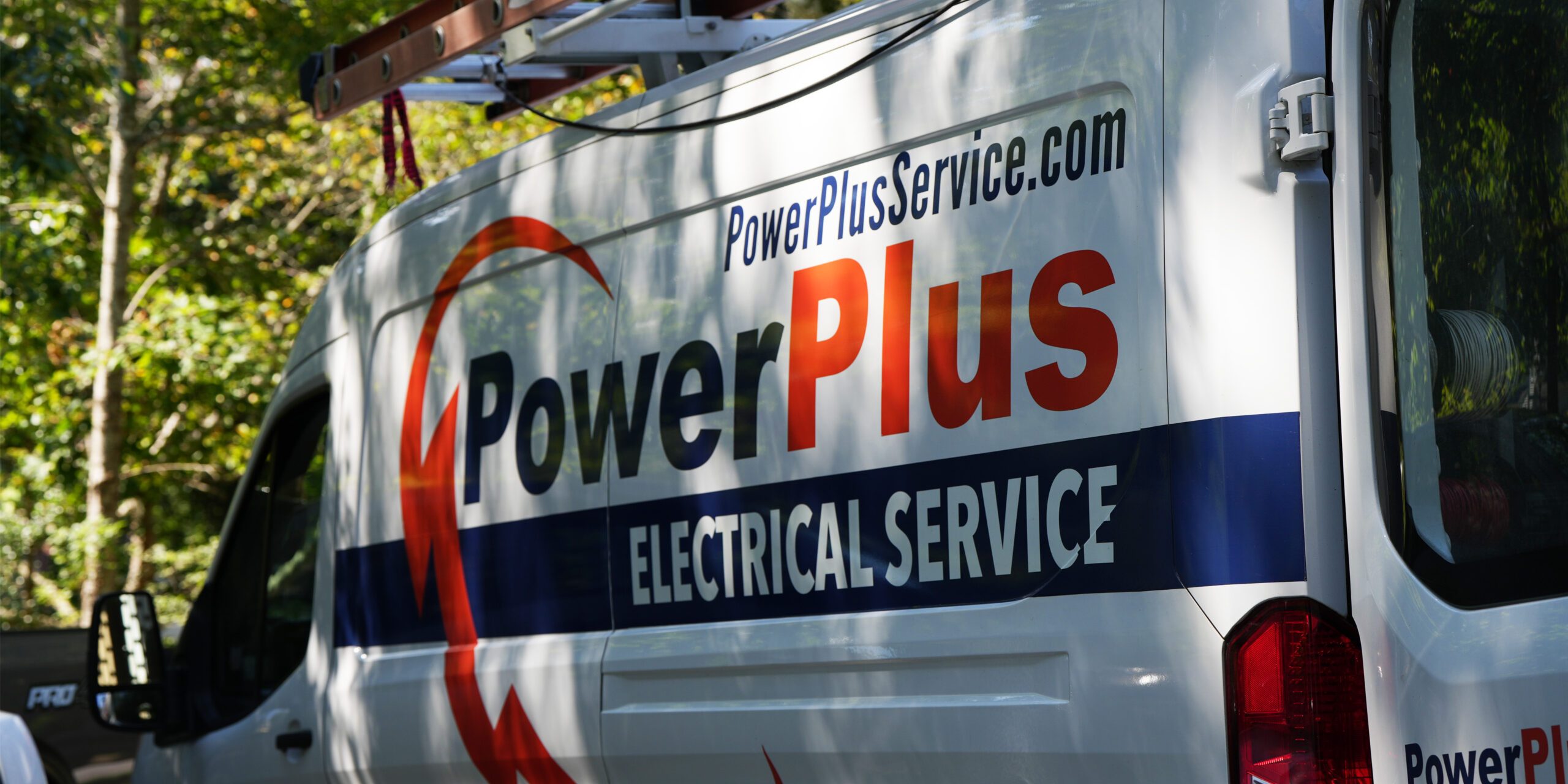 A white van with PowerPlus Electrical Service and a website address on its side is parked in a sunlit wooded area, reflecting the companys focus on blending traditional electrical work with modern web design and marketing. A ladder is secured on top of the van.